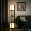 A tall black metal floor lamp with three illuminated white rectangular light panels, styled in a modern living room next to a gray sofa and a round side table.